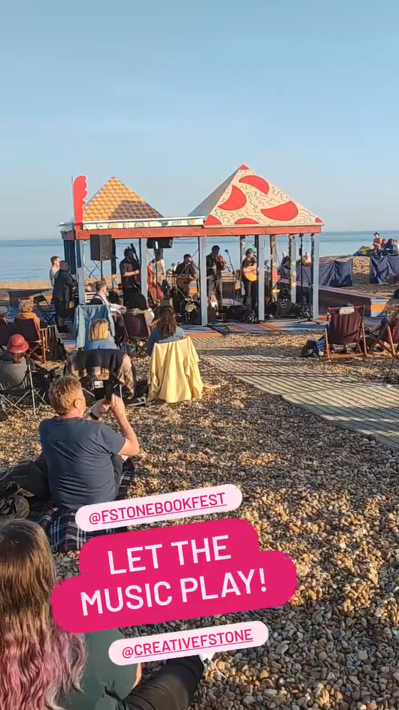 A band playing in a bandstand on a stony beach. 