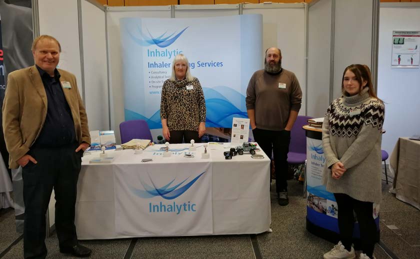 Four people standing at a table which has the companies logo on and information about what they do. 