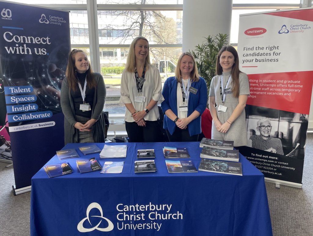 Four staff members from the Enterprise and Engagement team at Canterbury Christ Church University standing behind a table with brochures and leaflets on about what the team offers.