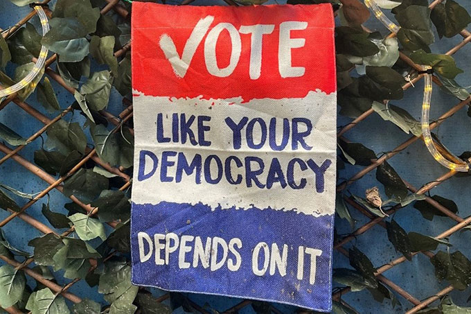 Poster on a fence with red, white and blue colours used reading "Vote like your democracy depends on it".