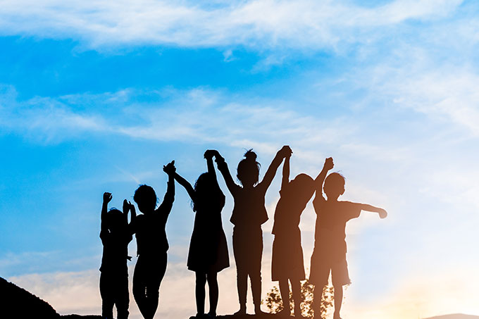 Children holding hands aloft silhouetted against the sky