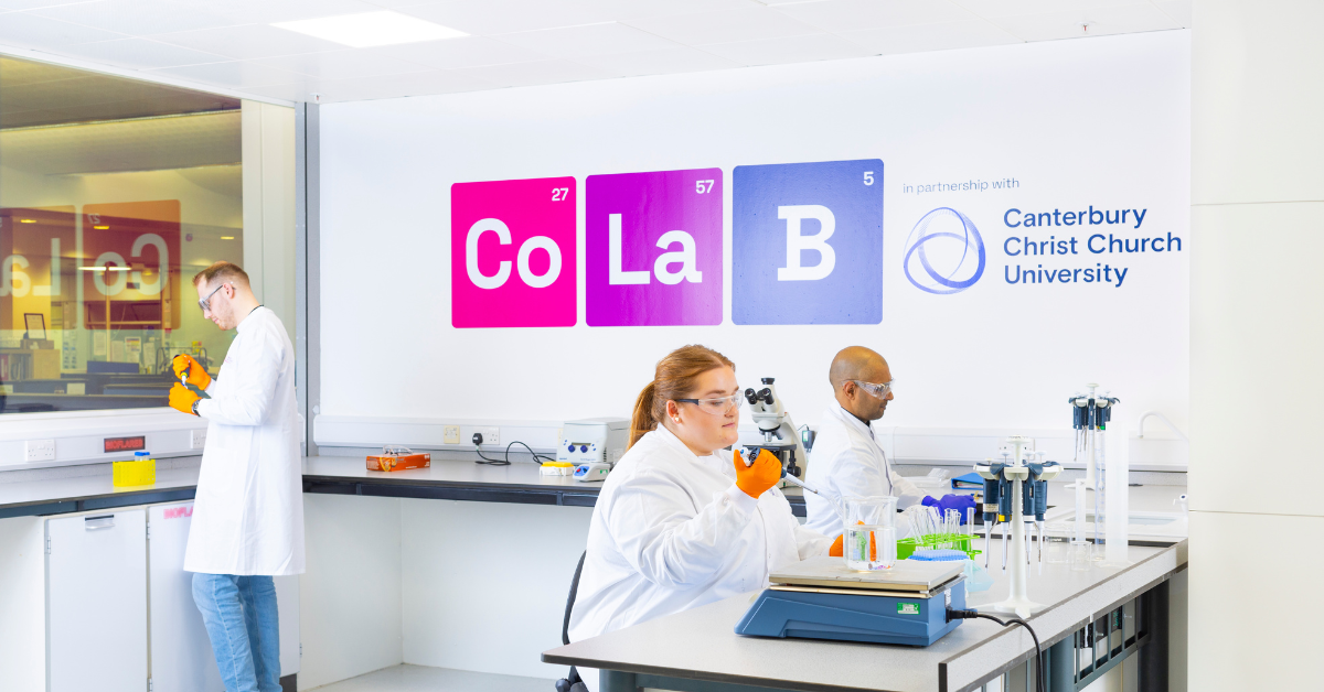 Three workers in la coats sitting in a lab with microscopes
