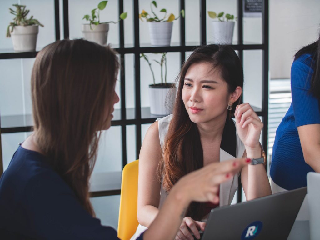 Two women talk while sitting in front of a laptop computer. 