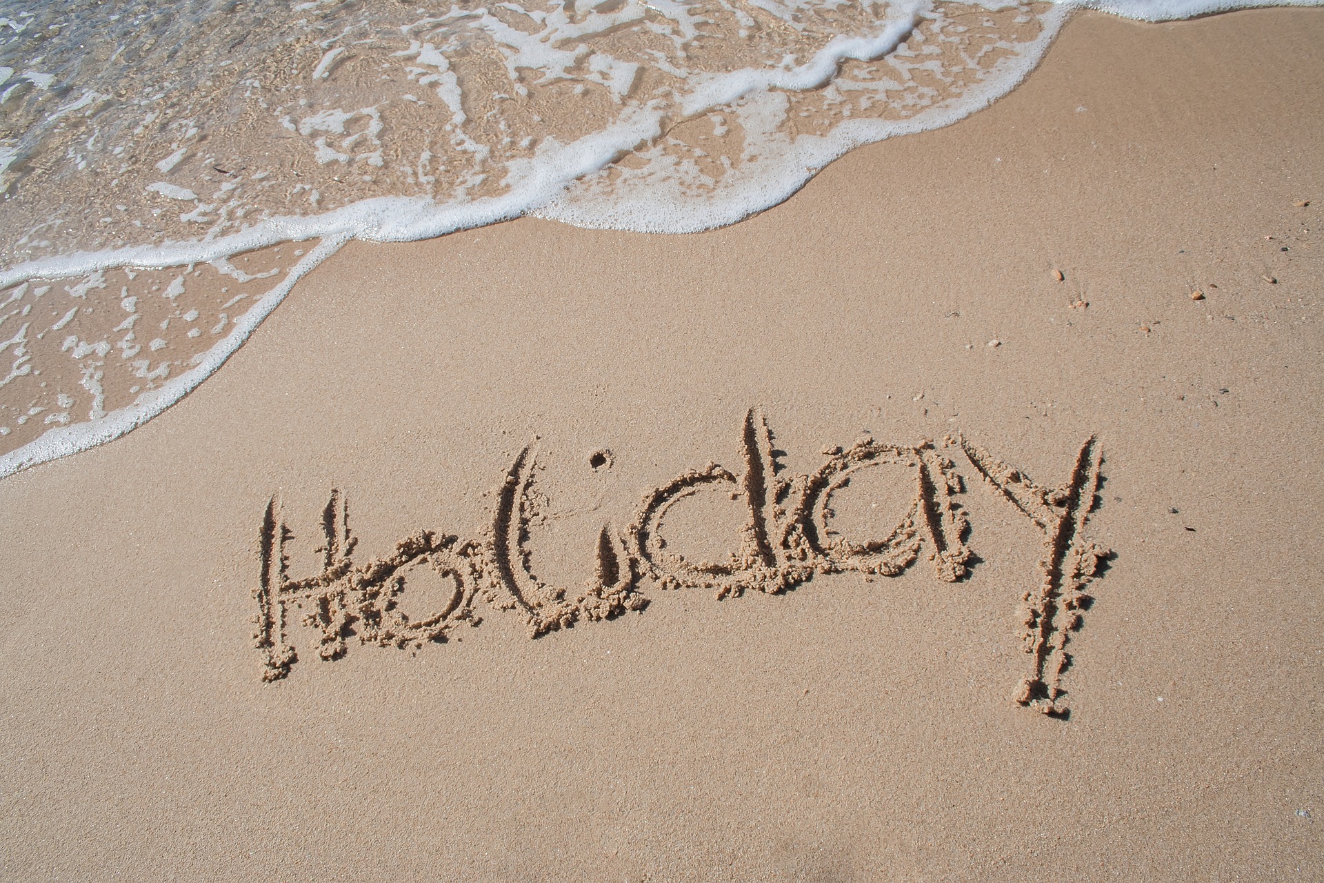 The words "Holiday" written in the sand on a beach.