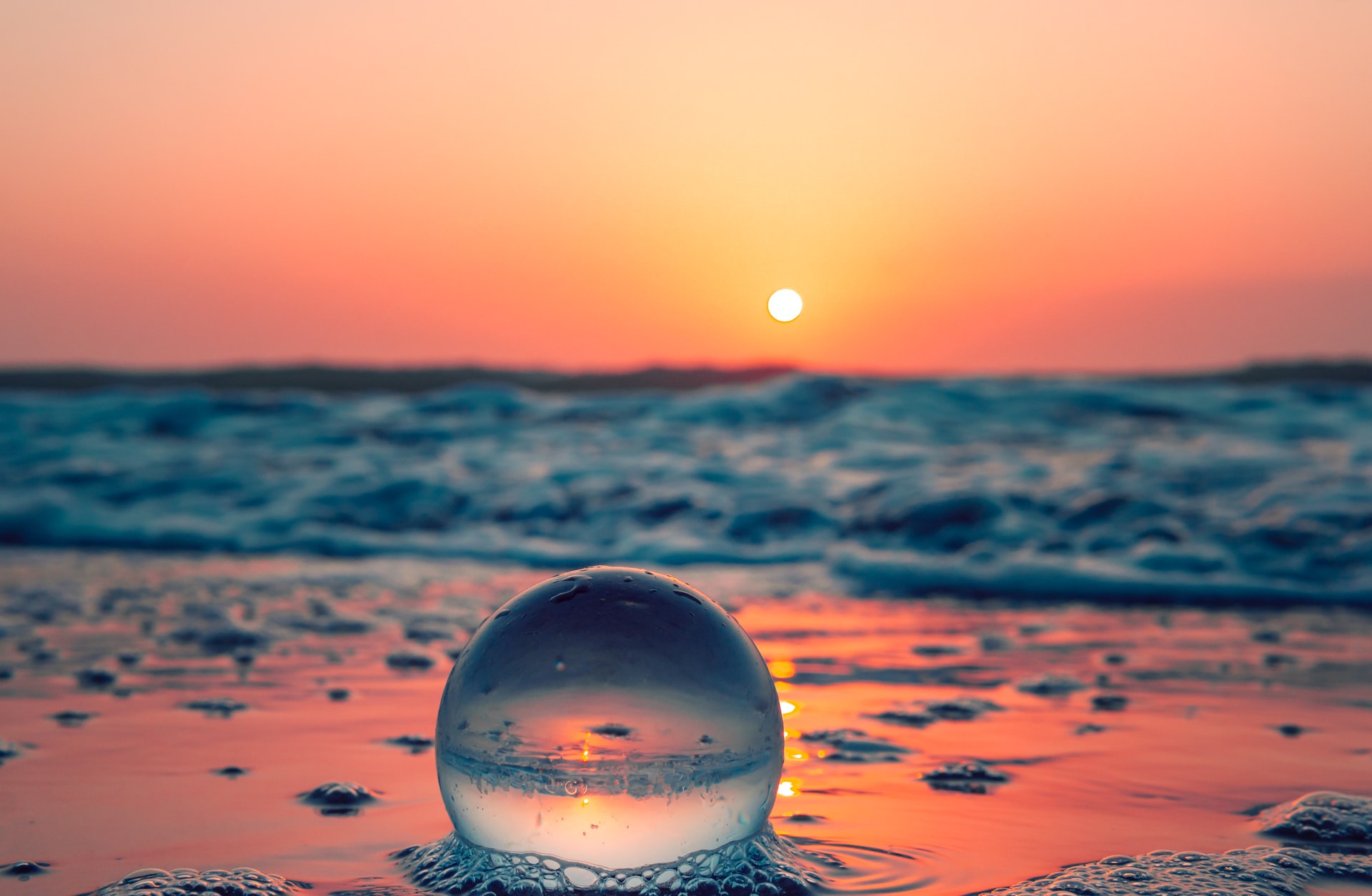 A foamy bubble on the beach, with the ocean in the background and the sun setting