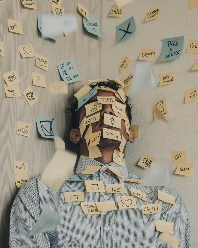 An exhausted male covered in post it notes - in front of a wall covered in post it notes