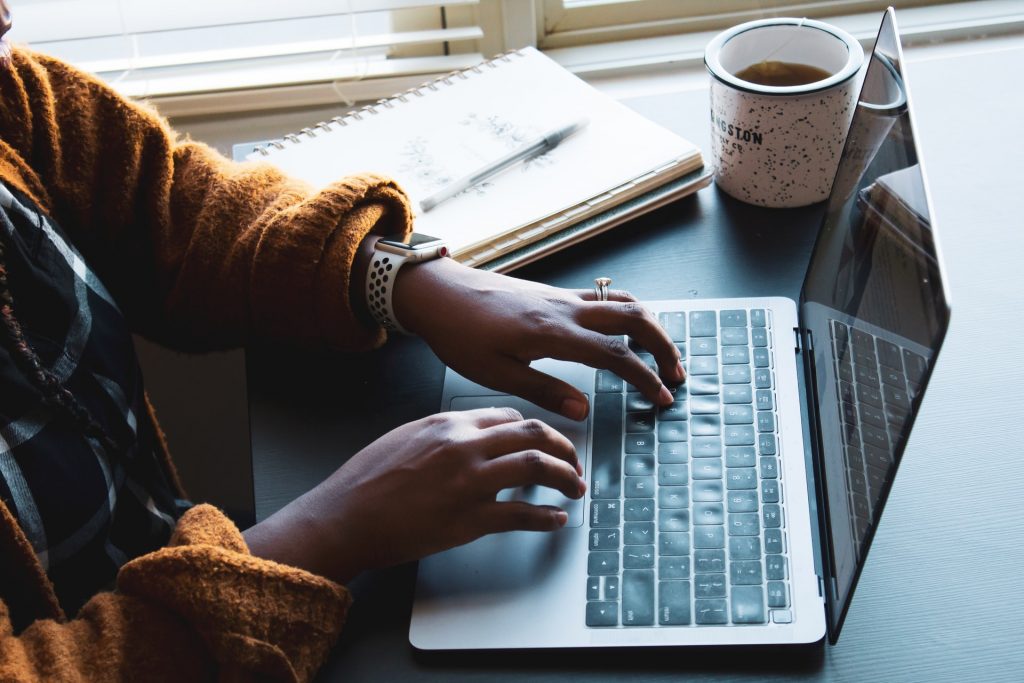 woman working on  her blog on a laptop with her notes and coffee to the side