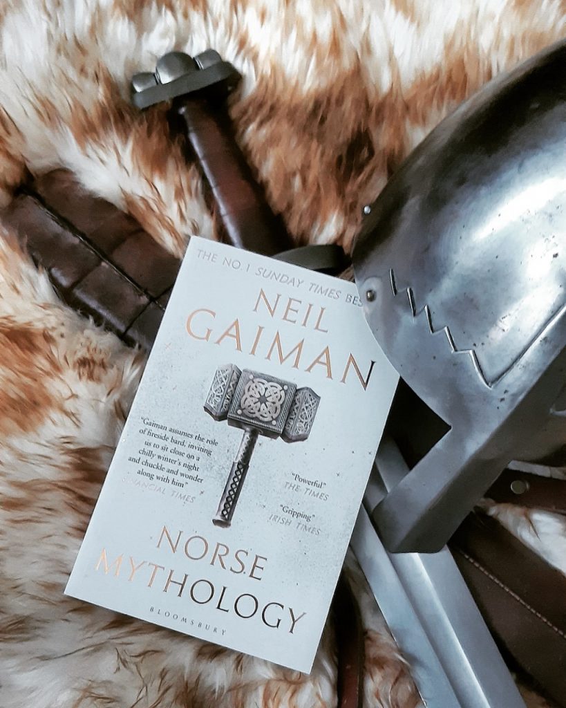 neil gaiman norse mythology book laying on viking furs, swords and helm