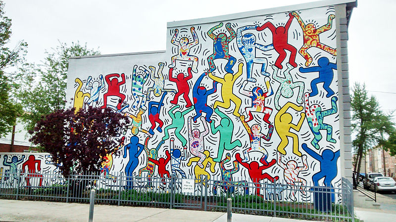 Colour photo of Keith Haring's mural 'We are the Youth' in Philadelphia. The mural features a large number of dynamic figures in different poses, some of which are filled with one colour and some of which are filled in with colourful patterns. 
