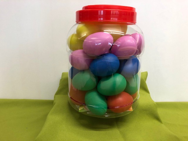 A large, clear tube with a red lid. Within the tub are 38 egg shakers of different colours.
