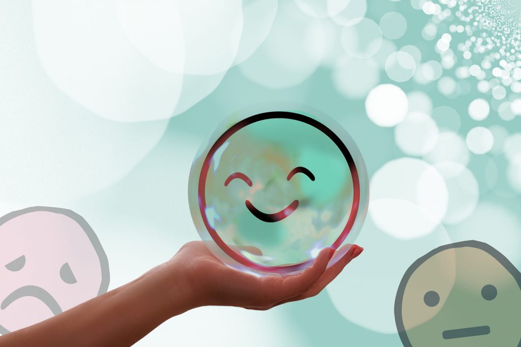 Hand holding a bubble with a happy face towards the sky. Either side are bubbles with sad faces.