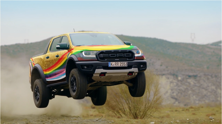 A Ford truck is mid-air and painted with a rainbow and gold glitter finish
