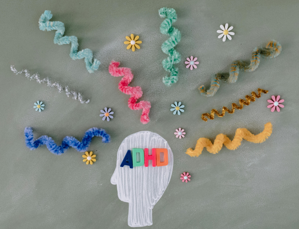 Arts and crafts design of a person's head with the word ADHD on it, and with colourful twirls and flowers coming out of it.