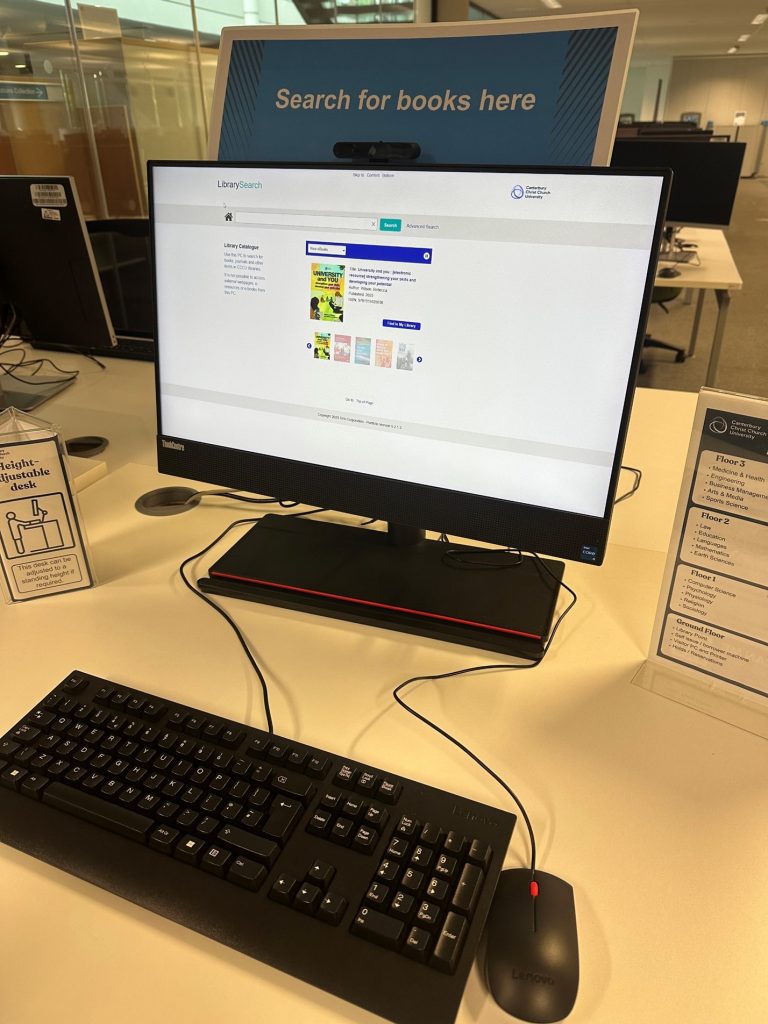 PC and keyboard on adjustable desk with a sign above saying 'Search for books here'