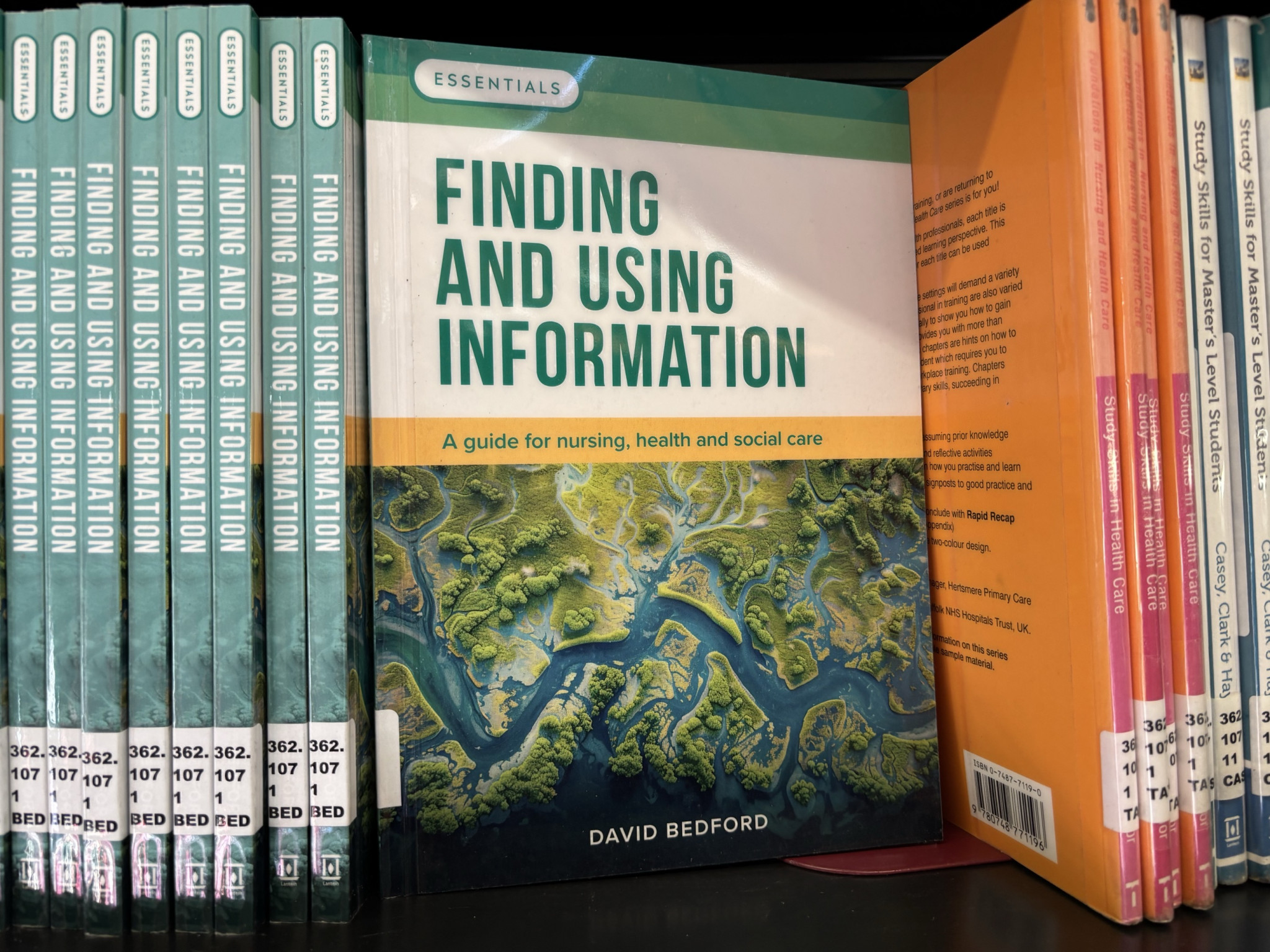 Books displayed on a shelf - copies of 'Finding and using information: a guide for nursing, health and social care' by David Bedford. The cover shows an overhead view of a river running through a verdant landscape.