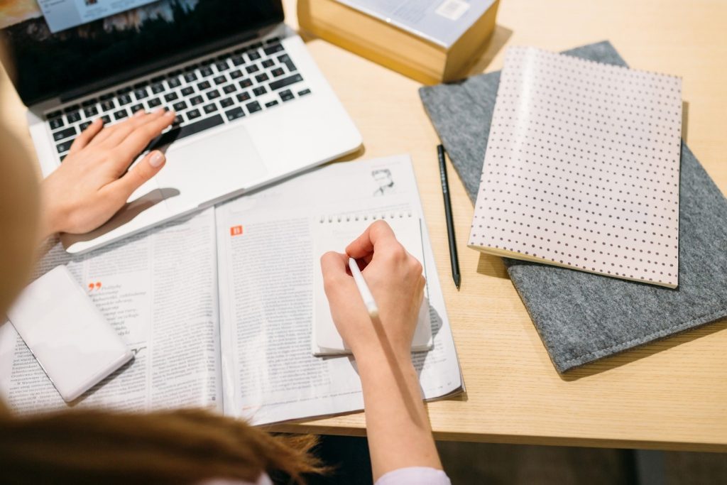 A person studying with a laptop in front of them and some notebooks.