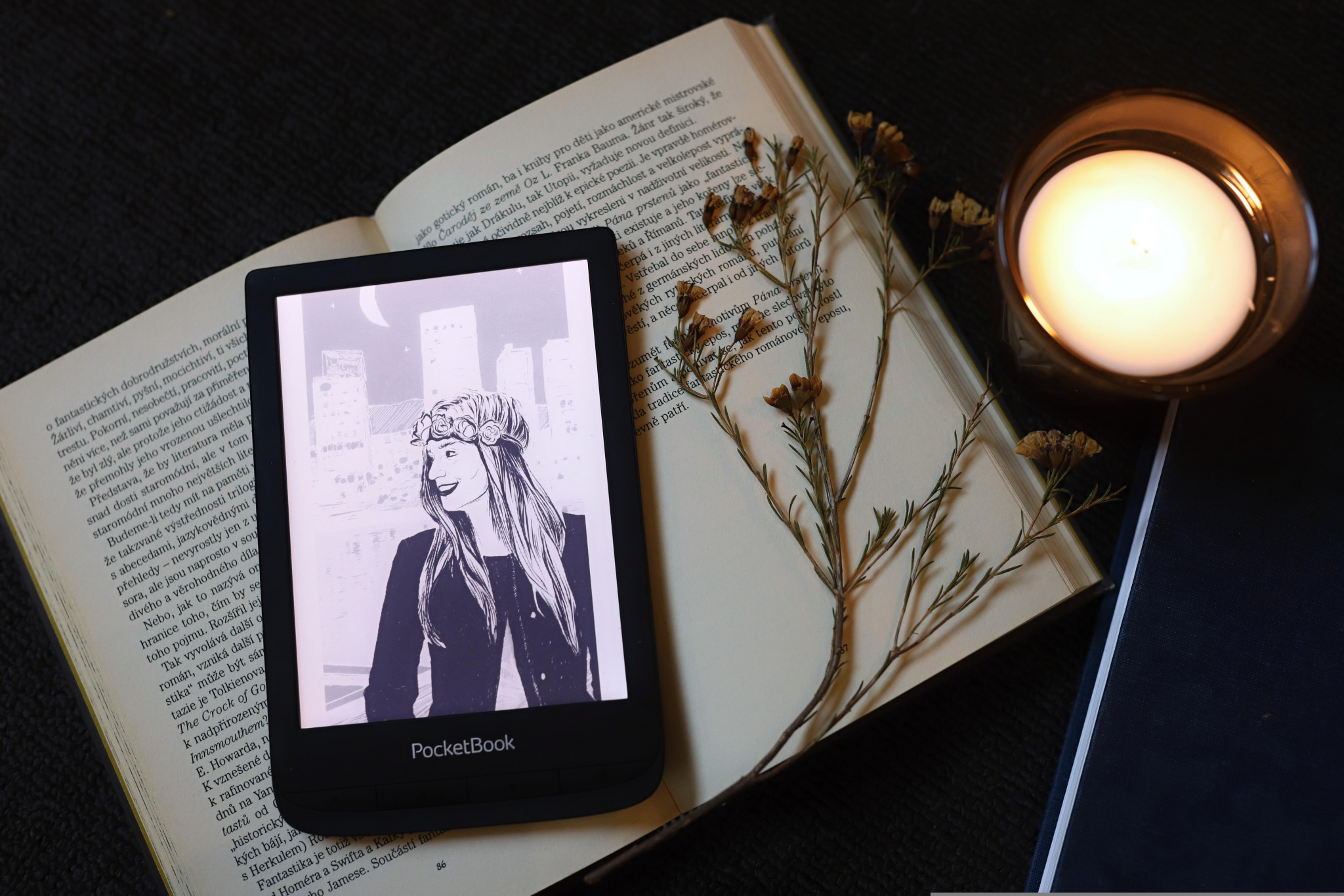 Tablet with e-book cover, sitting on an open book with flowers and a glass beside it
