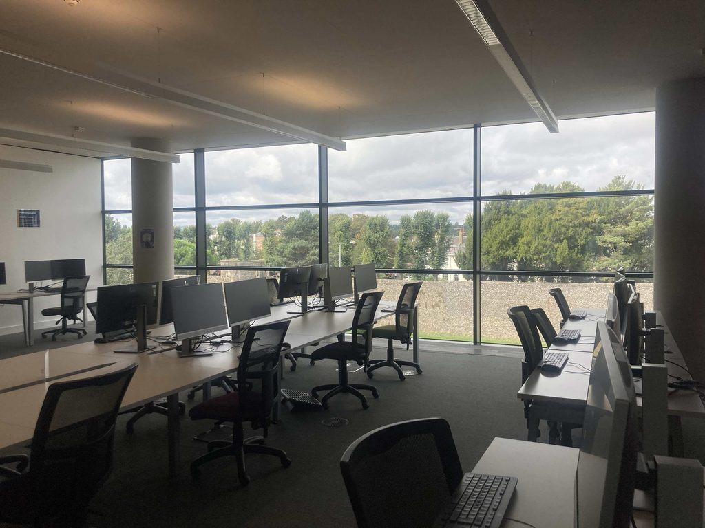A landscape shot of the front of our new Postgraduate Area, with more desks by a large window. 