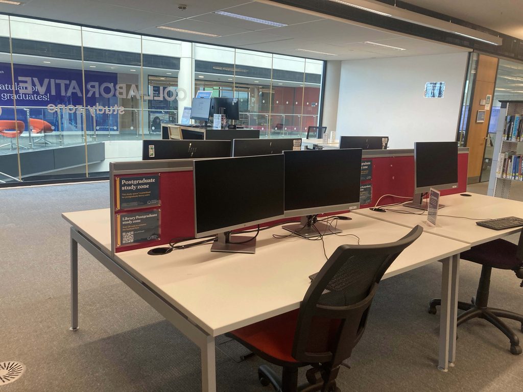 A close shot of the original Postgraduate Study Area's computers and signage on desks.