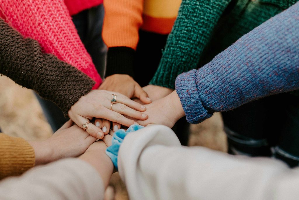 A group of people in colourful jumpers placing their hands on each others.