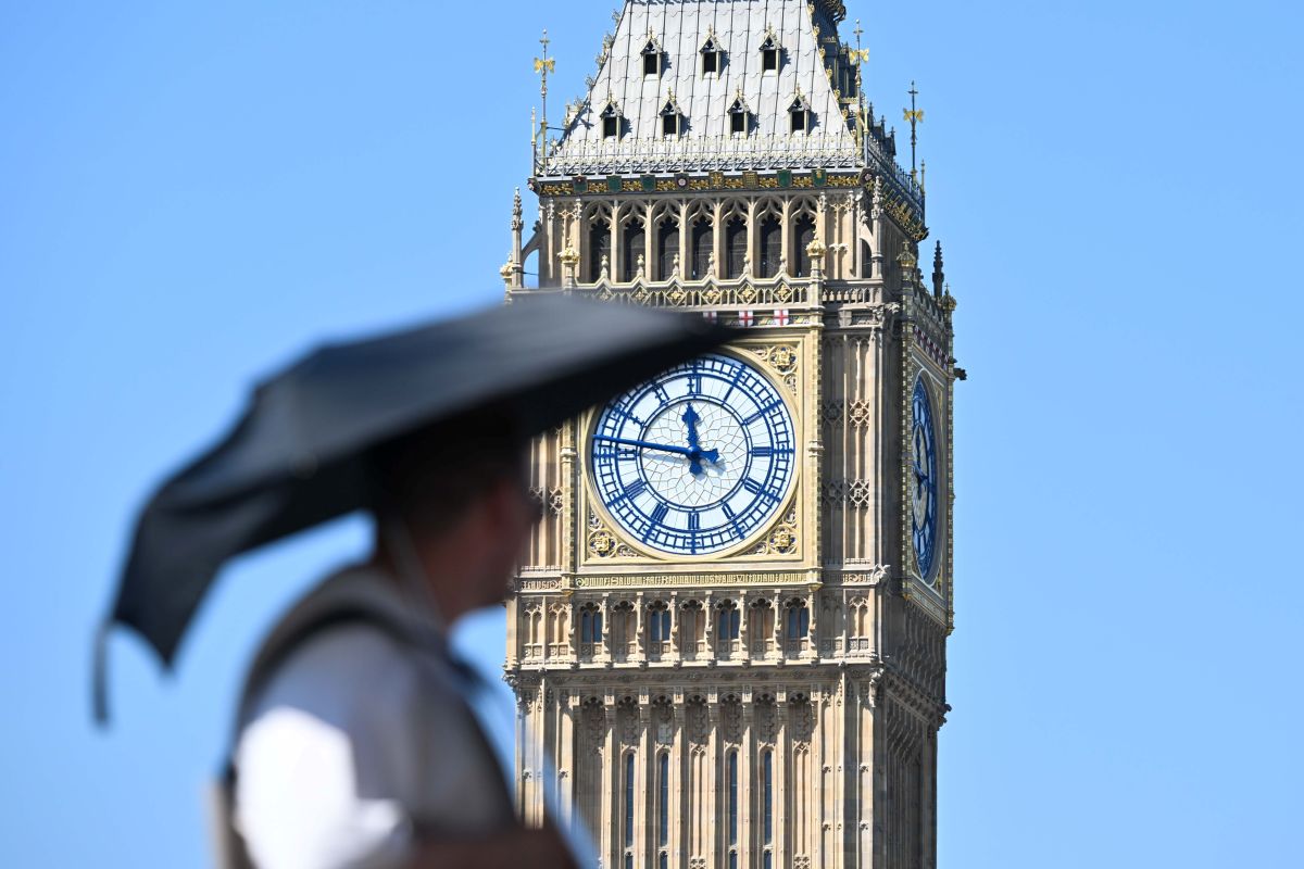 Man walking past Big Ben with umbrella for shade in heatwave