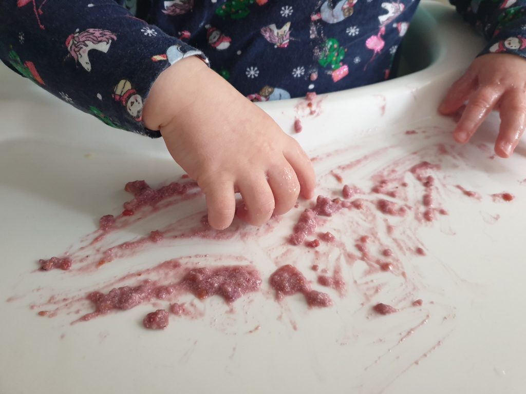 Child's hands playing with edible paint in a highchair