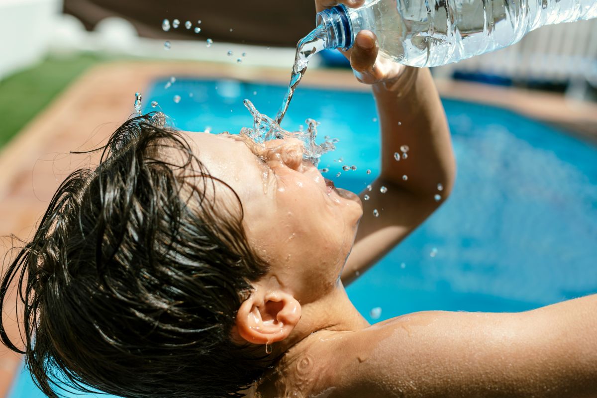 Boy by swimming pool throwing water on his face